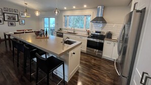 A modern kitchen with a central island, stainless steel appliances, and a large window providing natural light. - Close to Wineries, The Beach, trails, and Downtown (Penticton)