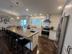 A modern kitchen with a central island, stainless steel appliances, and a large window providing natural light. - Close to Wineries, The Beach, trails, and Downtown (Penticton)