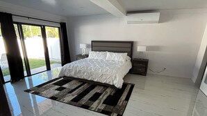 Une chambre moderne avec un grand lit, un sol en marbre et une vue sur l’extérieur grâce à une porte coulissante.