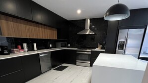 Une cuisine moderne avec des meubles de couleur noire, un sol en marbre blanc, des appareils en acier inoxydable et un luminaire suspendu noir.