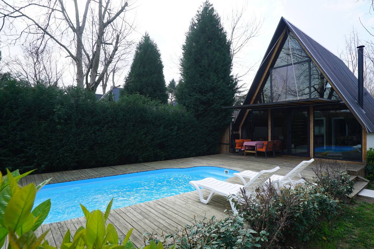Een modern huis met een zwembad, een houten terras en een serre.
