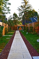 A pathway leading to a wooden gate with a triangular archway, surrounded by a well-maintained garden with trees and shrubs.