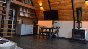 A cozy cabin interior with a wooden ceiling, a dining area with a table and chairs, a kitchen with cabinets and a stove, and a lofted sleeping area with a ladder. - Big garden sapanca (Sapanca)