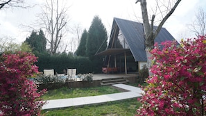 Een modern huis met een schuin dak, een terras en een tuin met roze bloeiende planten.