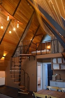 A loft-style room with a wooden ceiling, a spiral staircase, and a kitchen area.