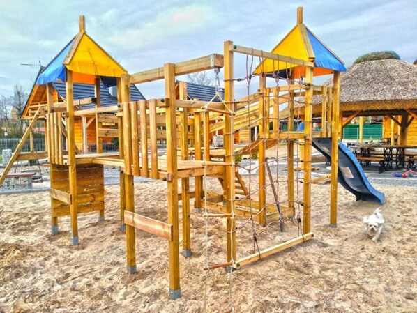 A wooden playground structure with climbing elements and a slide, set on sandy ground. - Comfortable Holiday Cottages Right by the Lake (Lubrza)