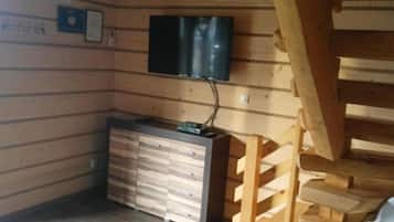 Una habitación con interiores de madera, un televisor de pantalla plana montado en la pared, una escalera de madera y un mueble con cajones.