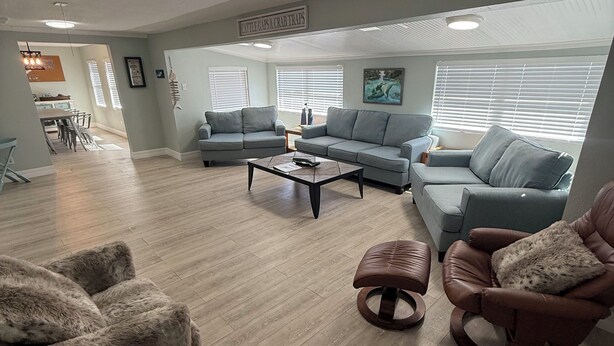 Un salón amplio con piso de madera, sofás grises, una mesa de centro y un sillón de cuero.