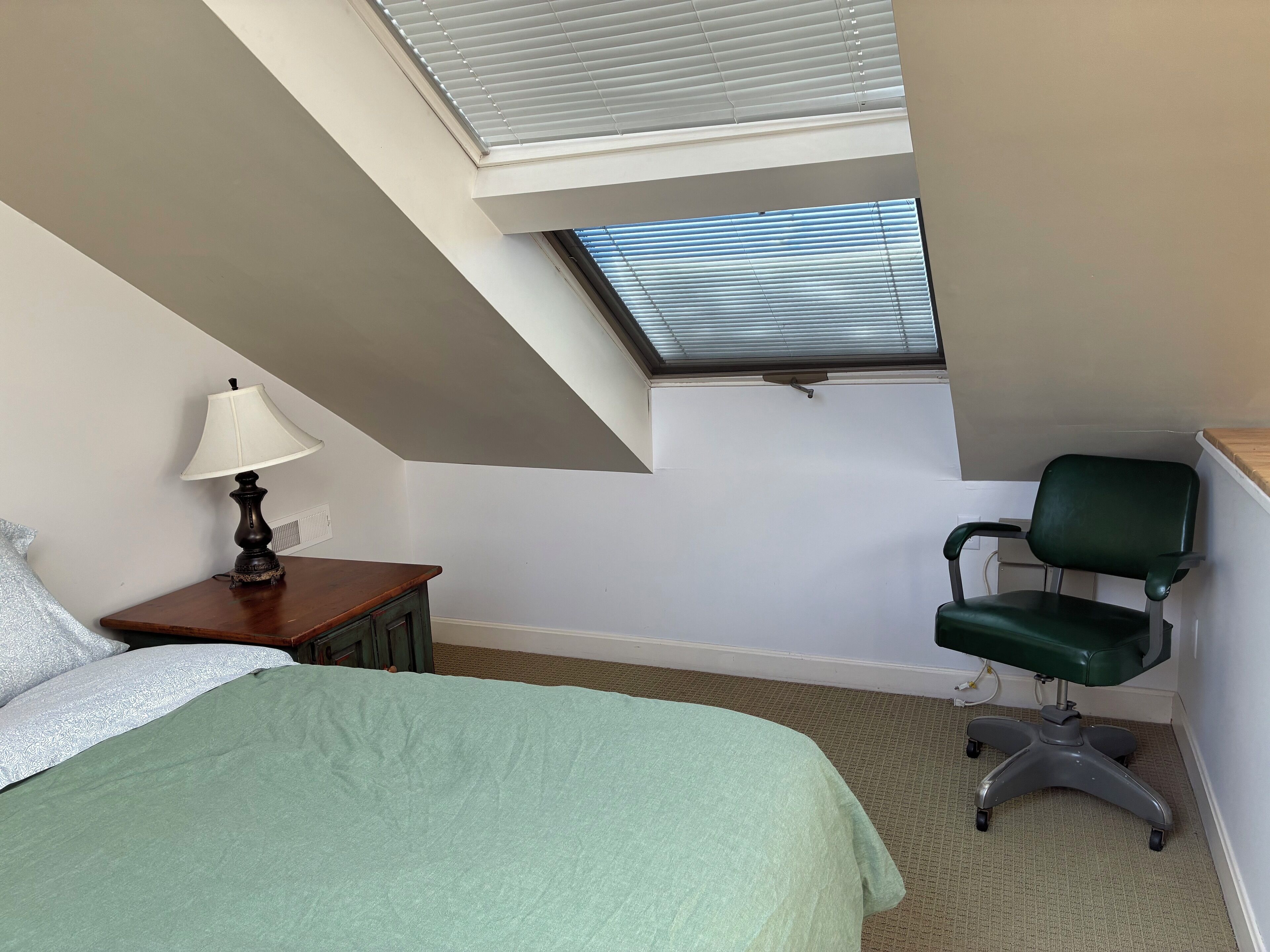 Une chambre à coucher avec une lucarne, un lit, un bureau avec une chaise et une lampe.