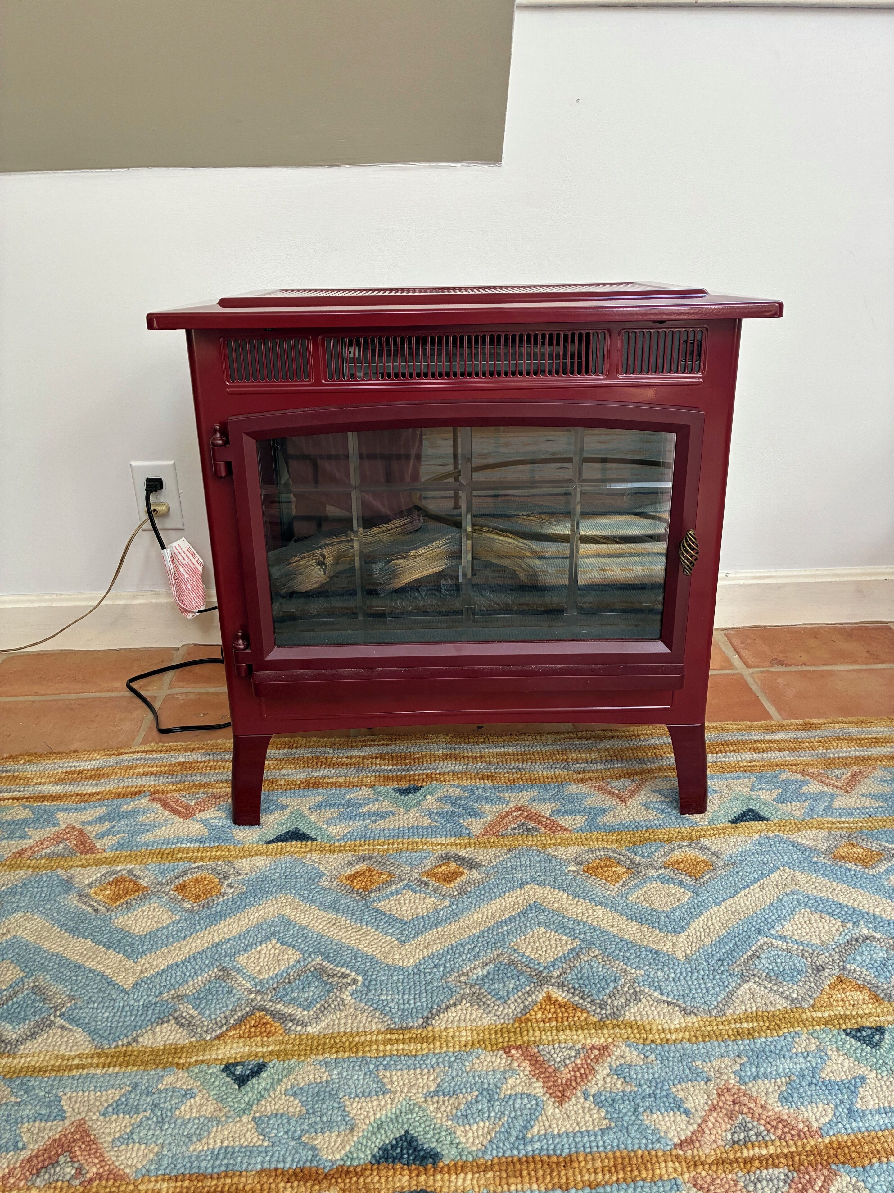 A red wooden cabinet with a glass door, placed on a patterned rug.