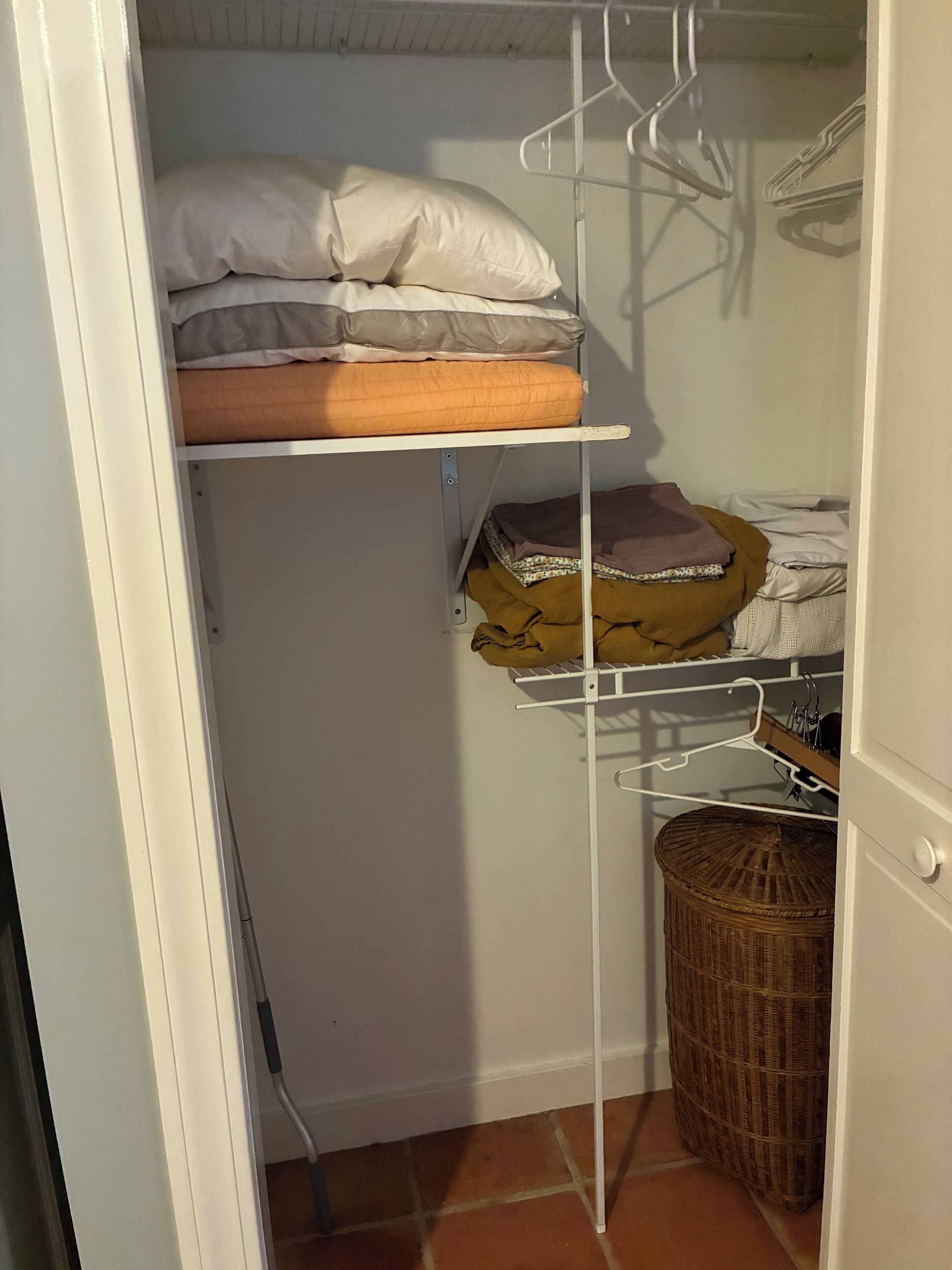 A storage closet with shelves, a wicker basket, and a hanging rack.