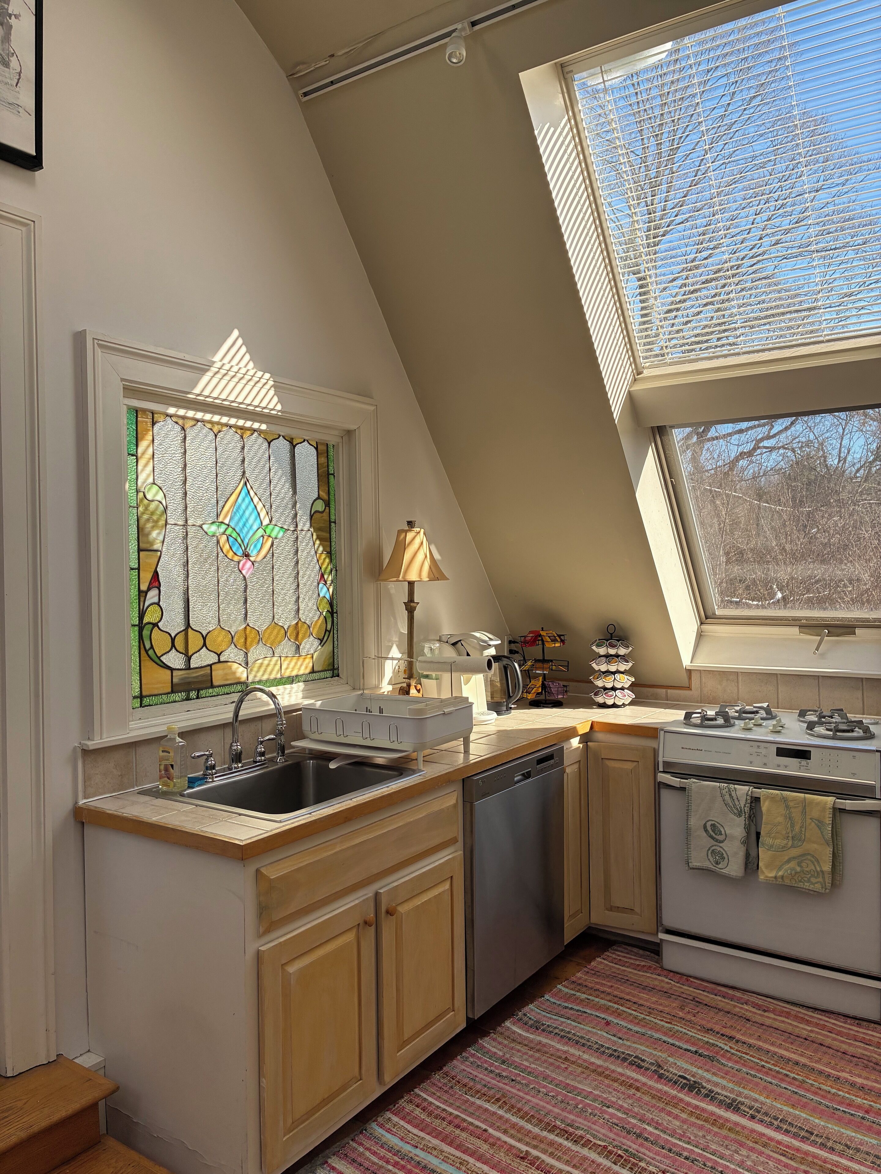 Una cocina con tragaluz, estufa, lavavajillas y ventana con diseño de vitral.