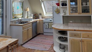 Una cocina con tragaluces, estufa, pileta y comedor con mesa y sillas.