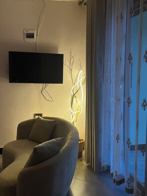 Uma sala de estar moderna com televisão de tela plana na parede, luminária elegante e um sofá confortável.