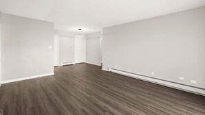 Una habitación amplia y vacía con suelo de madera y paredes blancas.