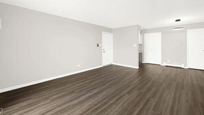Una habitación amplia y vacía con suelo de madera y paredes blancas.