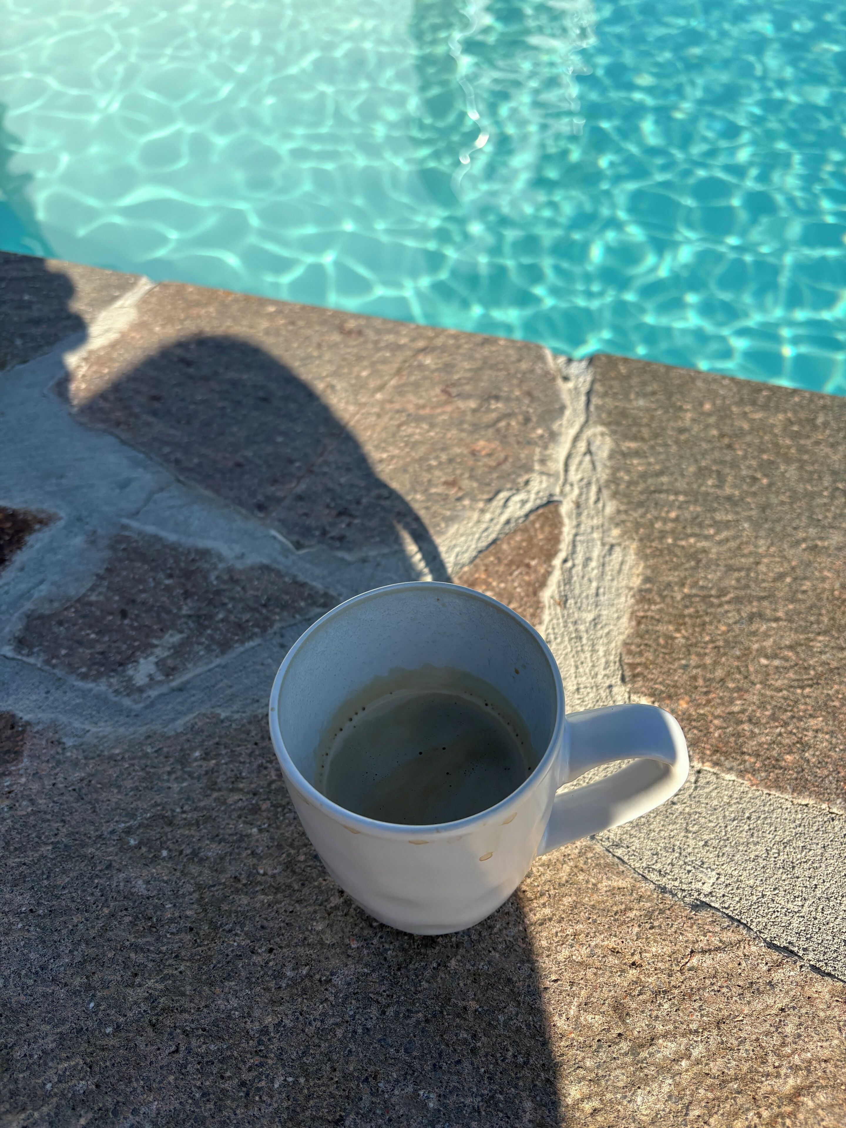 A white mug on a stone surface by a pool with clear water.