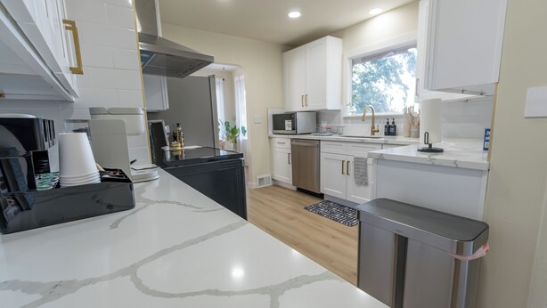 A modern kitchen with white cabinets, a stainless steel sink, and a marble countertop. - Spacious 7BR 4BA Home - Game Room - AC/Heat - 20 min to Airport (Kent)