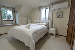 A bedroom with a large bed, a bedside table, a lamp, and a window with curtains.