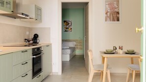 A compact kitchen with a dining area, a bed in the adjacent room, and a poster on the wall. - Cozy 1-bedroom house in the charming historic center of Noto (Noto)