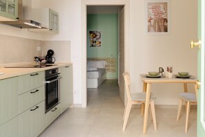 A compact kitchen with a dining area, a bed in the adjacent room, and a poster on the wall. - Cozy 1-bedroom house in the charming historic center of Noto (Noto)