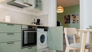 A compact kitchen with a built-in oven and washing machine, a wooden dining table, and a hanging light fixture. - Cozy 1-bedroom house in the charming historic center of Noto (Noto)