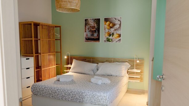 A neatly made bed with white linens and two pillows, a wooden wardrobe, and two wall-mounted lamps. - Cozy 1-bedroom house in the charming historic center of Noto (Noto)