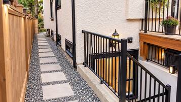 A narrow pathway with stepping stones leading to a building with a wooden fence on one side and a black metal railing on the other.