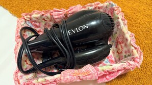 A black hair dryer with the brand name EVLON, placed on a floral-patterned cloth with a pink bow. - Stylish 2BR Suite 2 Queen Beds 20 Min to YVR (Vancouver)