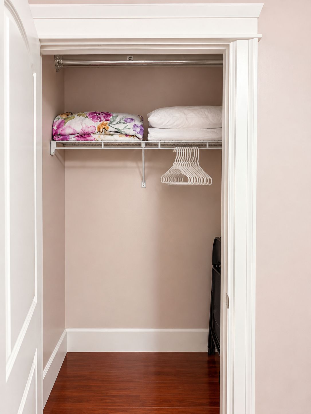 A closet with a wooden floor, a hanging rack, and a shelf with folded bedding.