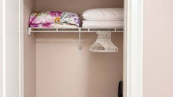 A closet with a wooden floor, a hanging rack, and a shelf with folded bedding.