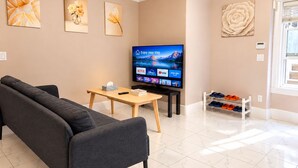 A modern living room with a sofa, a coffee table, a flat-screen TV, and a shoe rack. - Stylish 2BR Suite 2 Queen Beds 20 Min to YVR (Vancouver)