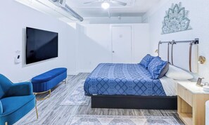 Une chambre à coucher avec un lit, une chaise bleue, un téléviseur et un ventilateur de plafond.