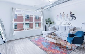 Ein modernes Wohnzimmer mit einem grauen Sofa, einem blauen Sessel, einem farbenfrohen Teppich und einer Wandmalerei.