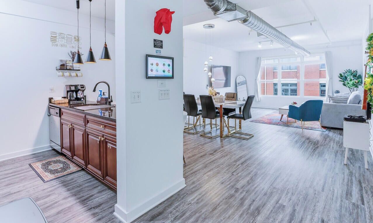 A modern kitchen with wooden cabinets, a coffee station, and a dining area with a table and chairs.
