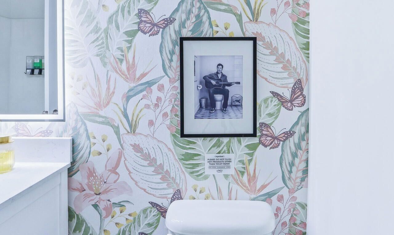 Une salle de bain avec un papier peint à motifs floraux, un tableau encadré au mur et des toilettes.