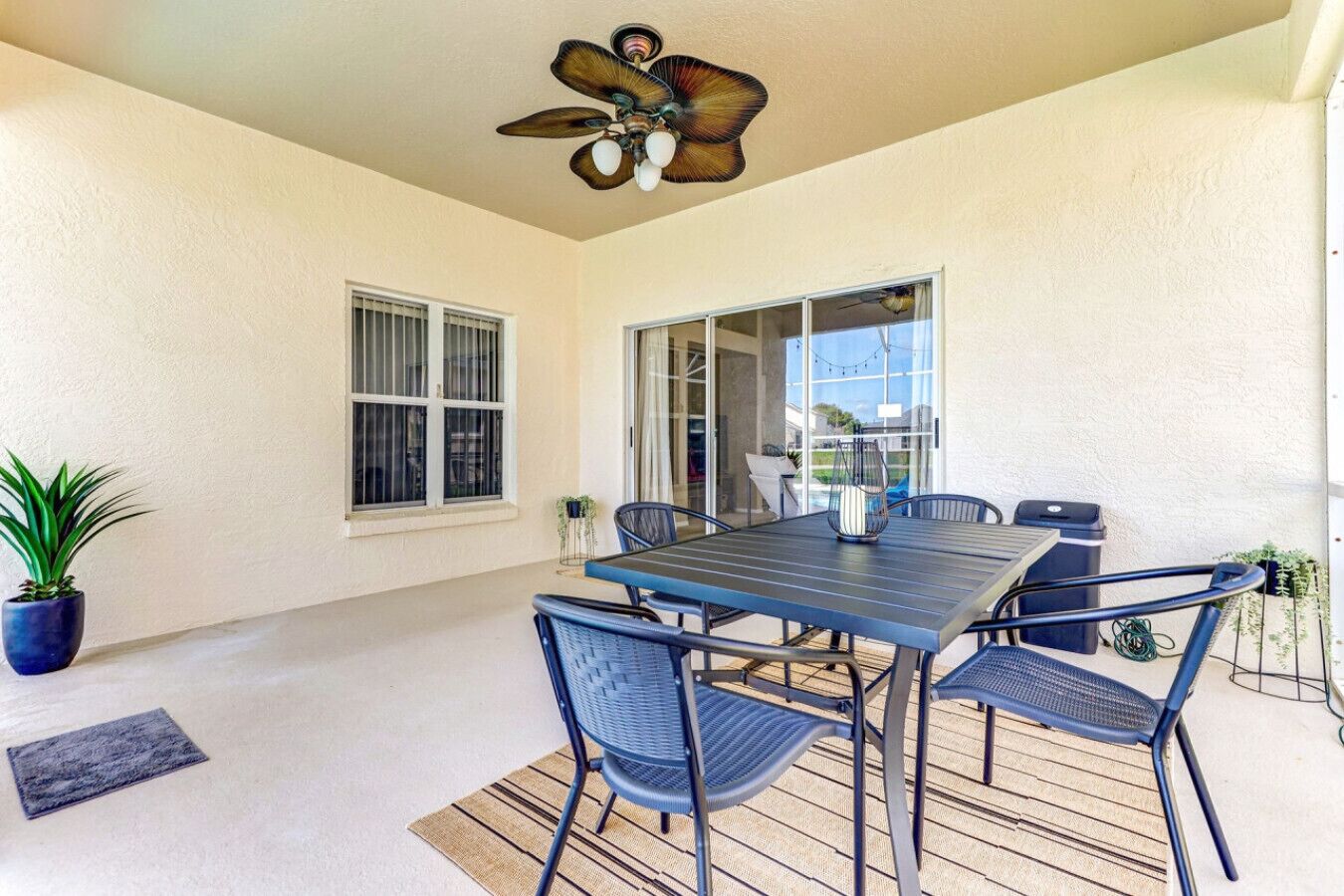 A covered patio with a table and chairs, a ceiling fan, and a potted plant.