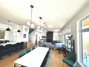 A modern kitchen with a large island, a dining area with a long table and chairs, and a living area with sofas and a fireplace. - La Galerie Charlevoix (Les Éboulements)