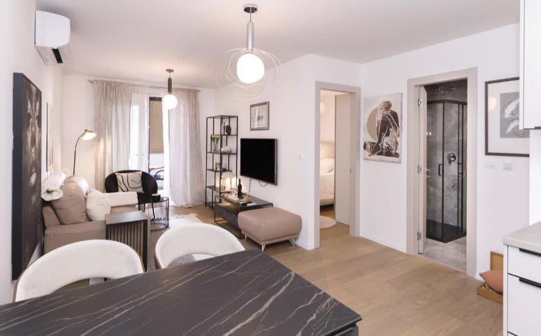 A modern living room with a sofa, dining table, and TV. There is a staircase leading to another room.