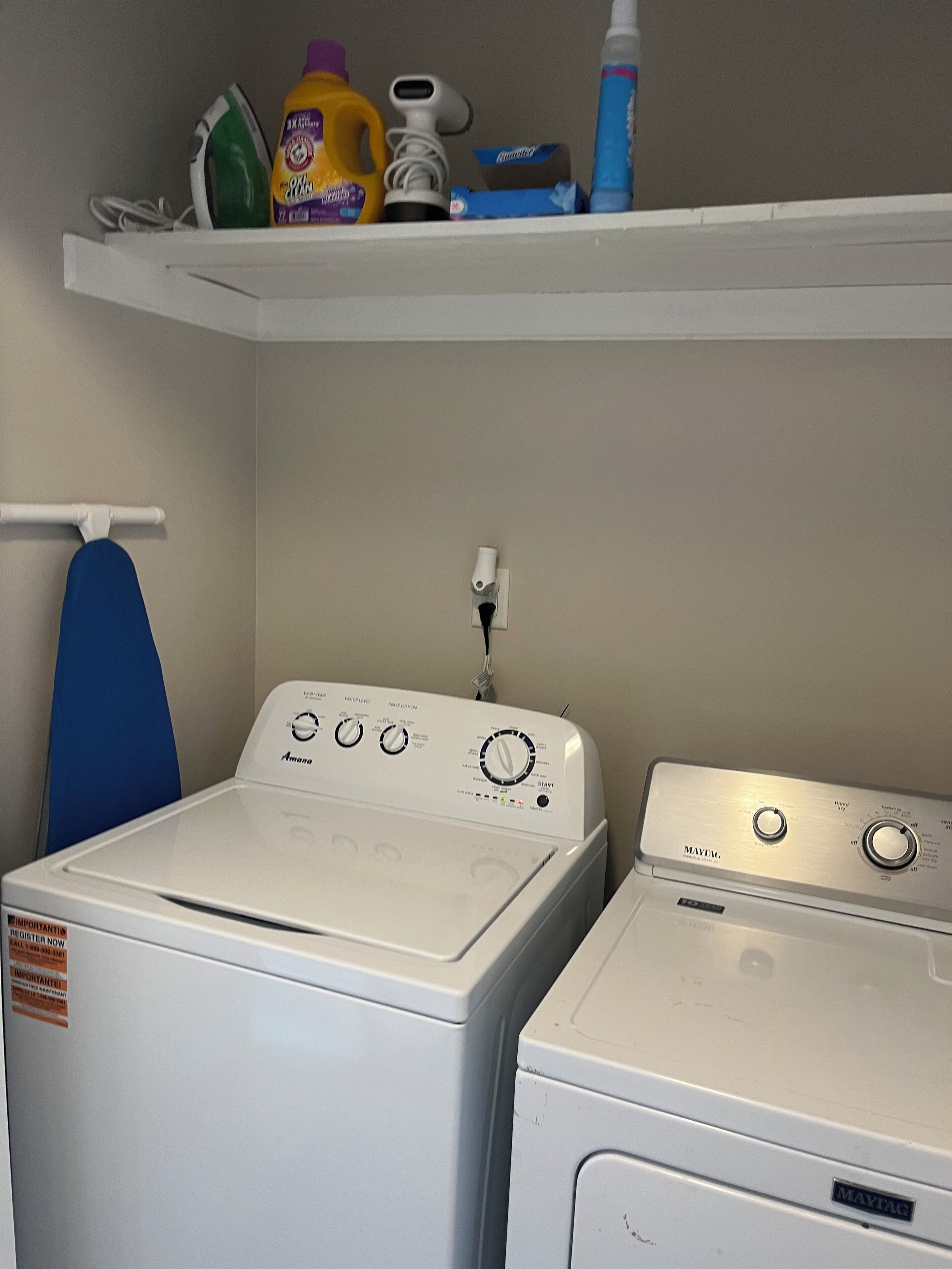 A laundry area with two washing machines, a drying rack, and a shelf with cleaning supplies.
