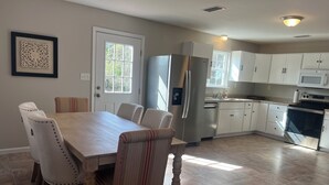 Una cocina moderna con armarios blancos, electrodomésticos de acero inoxidable y un comedor con mesa y sillas de madera.