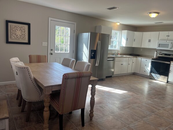 A modern kitchen with white cabinets, stainless steel appliances, and a dining area with a wooden table and chairs.