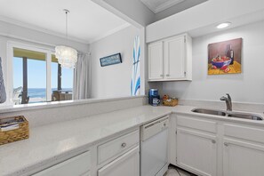 A kitchen with white cabinets, a double sink, and a view of the ocean through large windows.