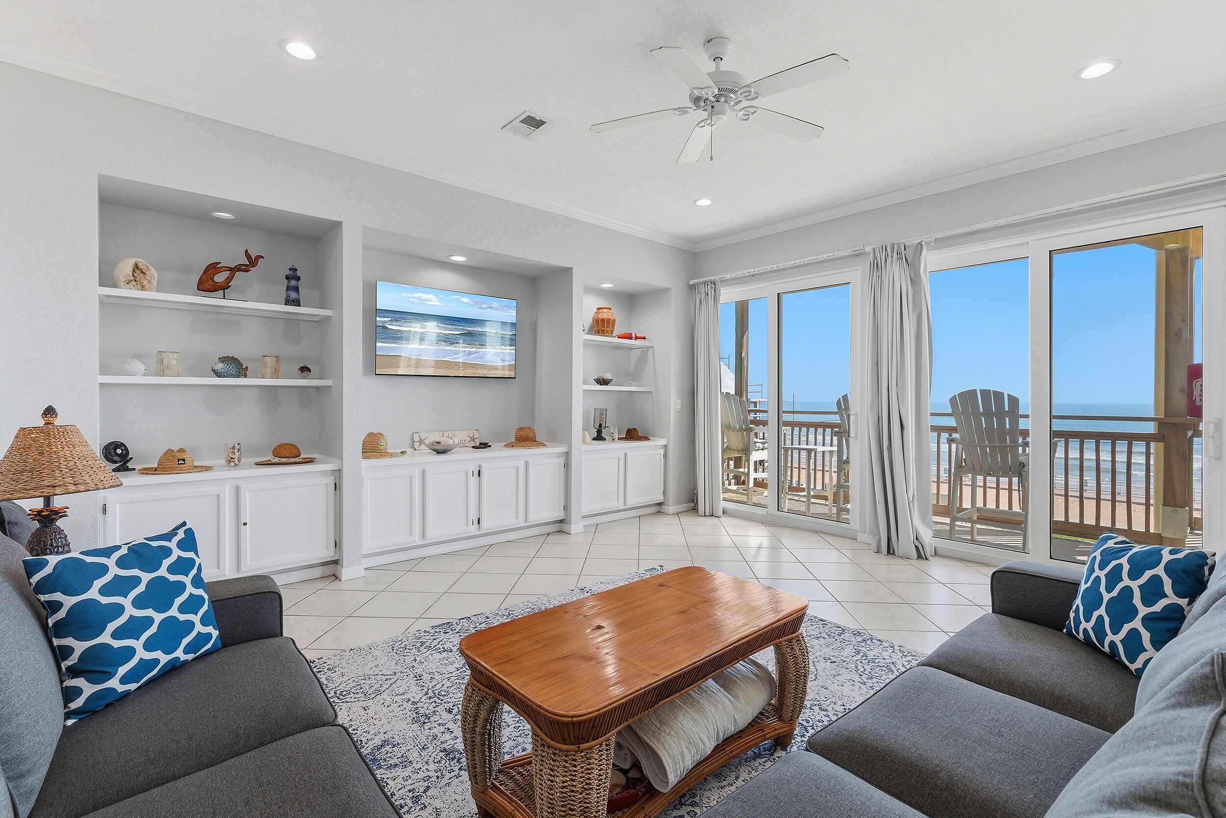A spacious living area with a view of the sea, white walls, and a ceiling fan.