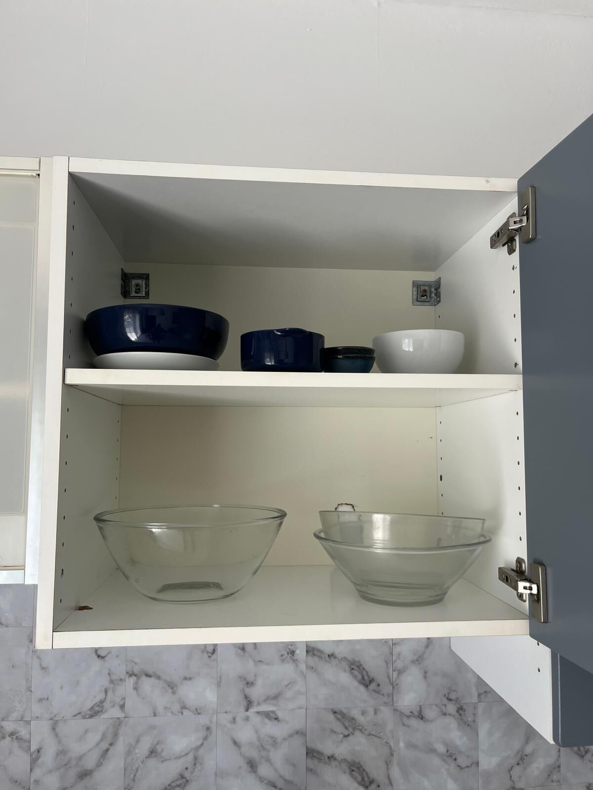 Un meuble de cuisine à deux étagères : l’une contient des bols bleus et blancs, et l’autre, des bols en verre transparent.