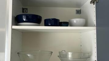 Un meuble de cuisine à deux étagères : l’une contient des bols bleus et blancs, et l’autre, des bols en verre transparent.
