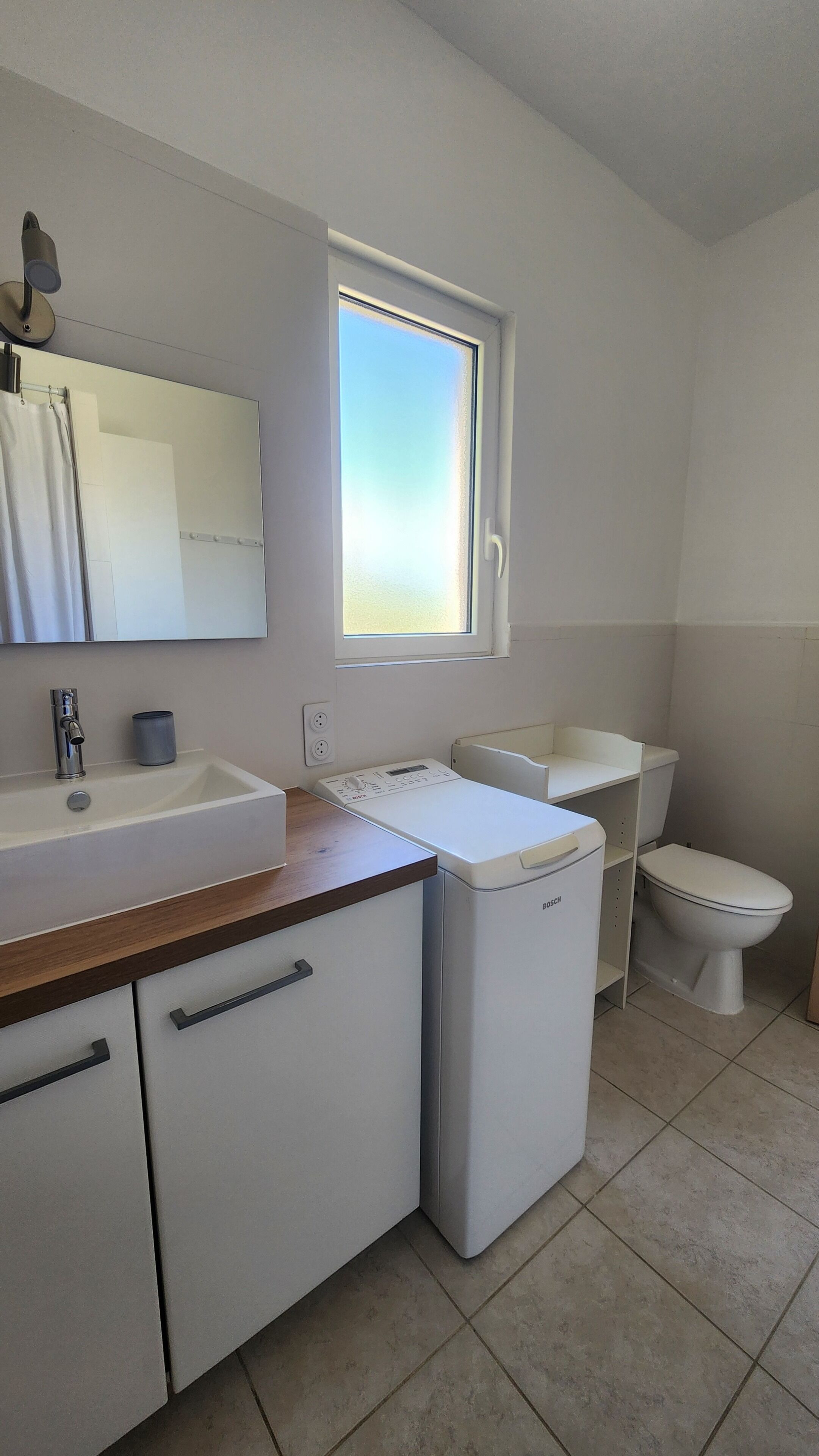 Une salle de bain avec un lavabo, un miroir, des toilettes et une fenêtre.
