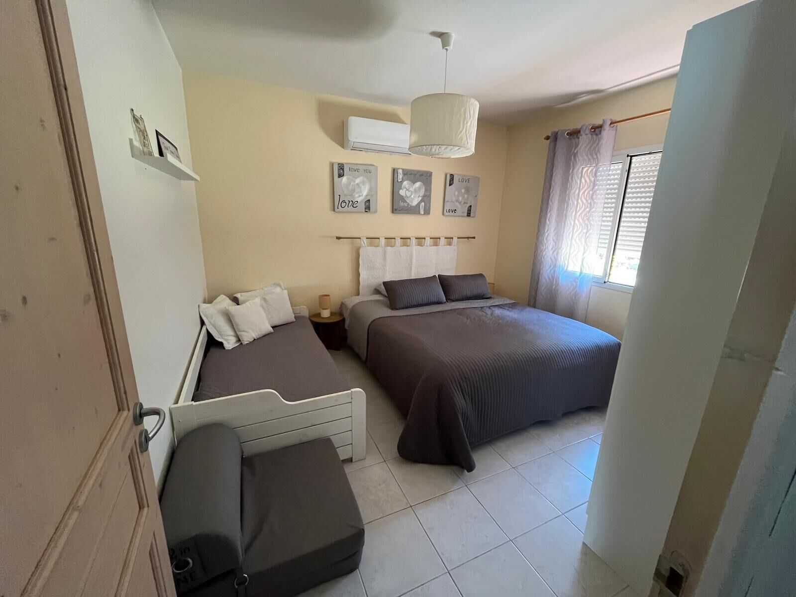 Une chambre avec deux lits, une table de chevet, une lampe et une fenêtre avec des rideaux.