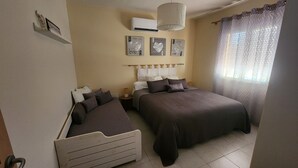 Un dormitorio con dos camas, ventilador de techo, unidad de aire acondicionado y una ventana con cortinas.