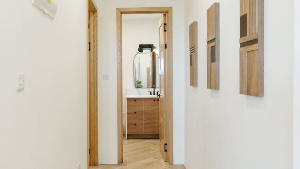 Un couloir au plancher de bois menant à une salle de bain équipée d’un lavabo et de meubles de rangement.